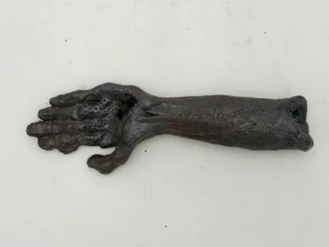 Dark ceramic forearm and open hand lying palm-up on a white surface.