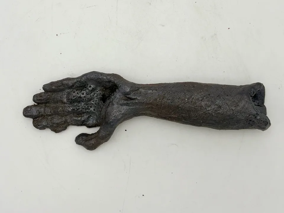 Dark ceramic forearm and open hand lying palm-up on a white surface.