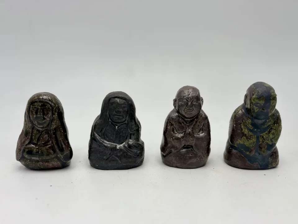 Four of the figures in a row: two hooded in dark glazes, a bald monk with folded hands, one mottled green.