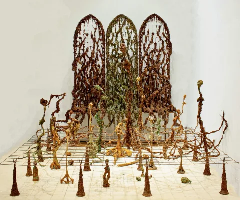 Installation of three arched lattice screens overgrown with root-like matter, standing over a grid field of thin sprouting figures.