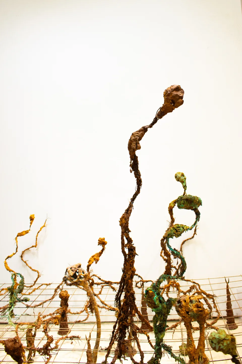 Detail: a tall stem with a crumpled head against the white wall, smaller figures rising around it.