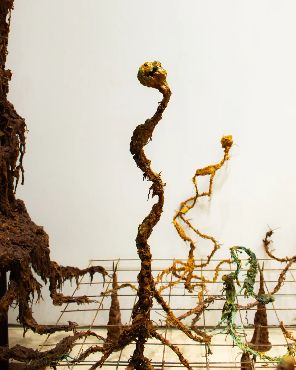 Detail: slender rust-coloured stems with bulbous heads rising from a wire grid, one tipped in green.