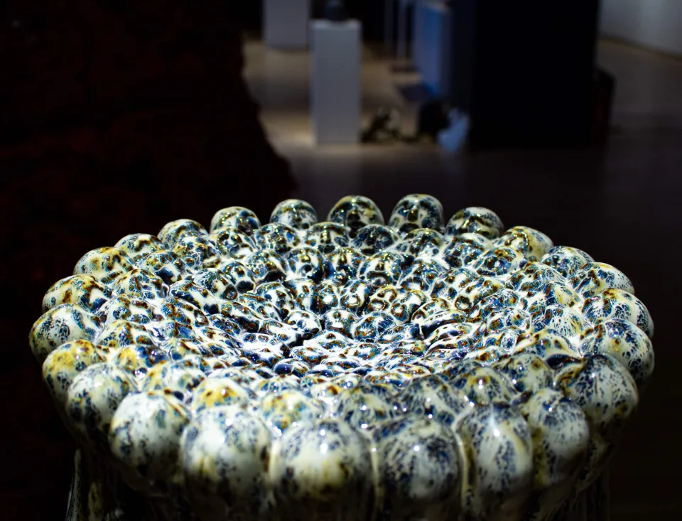 Glazed ceramic vessel crowned with a cluster of bulbous head-like forms, seen from above.