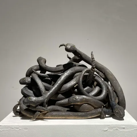Ceramic sculpture of dark snakes tangled into a single mound, several heads emerging outward.