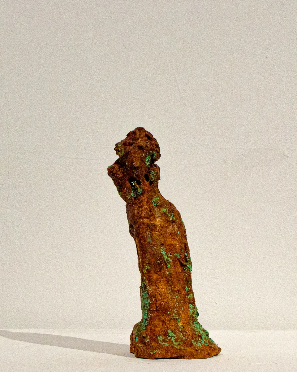 Small rust-coloured figure, its head tilted back, green oxidation blooming over the body.
