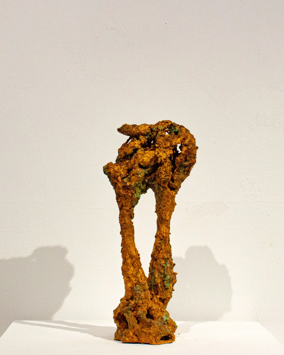 Small rust-coloured figure on two legs, its head a tangled, perforated mass.