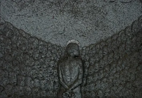 Ceramic relief triptych: a lone figure with hands bound behind its back, facing away, surrounded by a wall of small anonymous faces.