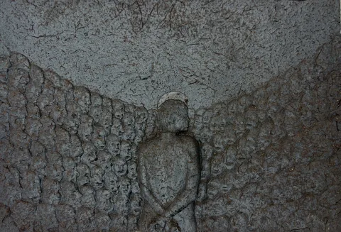 Glazed ceramic relief: a lone figure seen from behind, surrounded by a field of small anonymous faces.