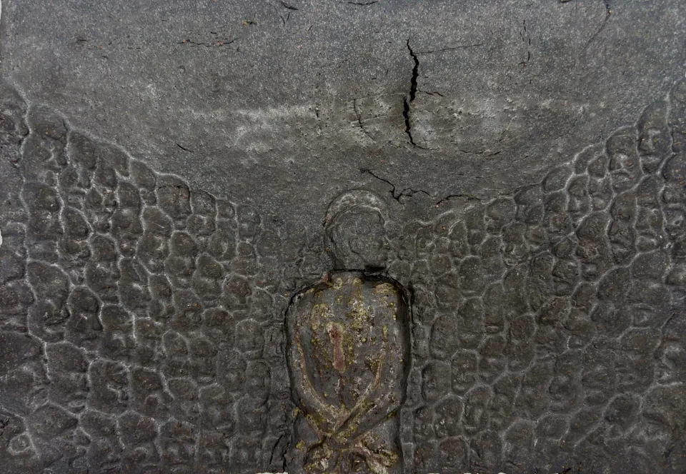 A second relief: the figure with hands bound behind its back, pressed into a cracked, scale-like surface.